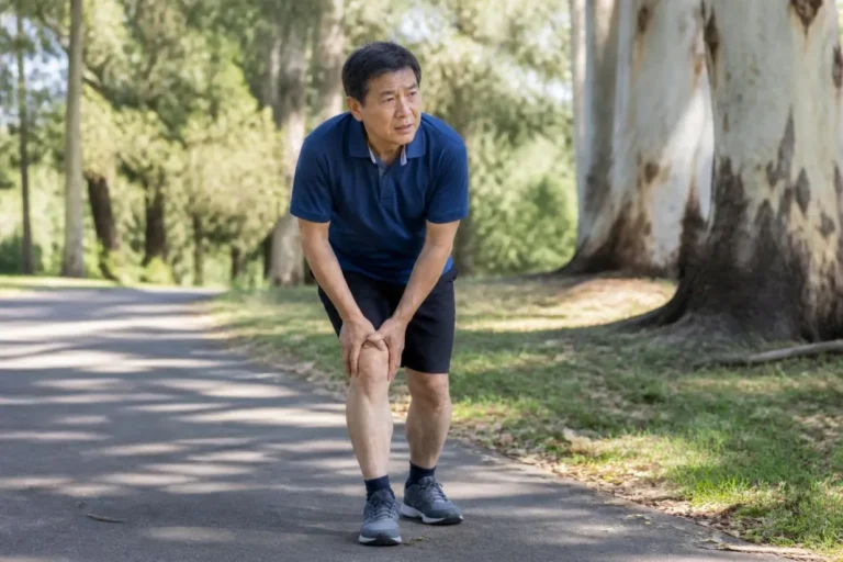 Man pausing on a park path and holding his sore knee