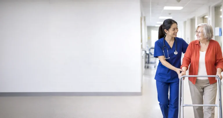 Nurse helping a patient walk with a frame after joint replacement